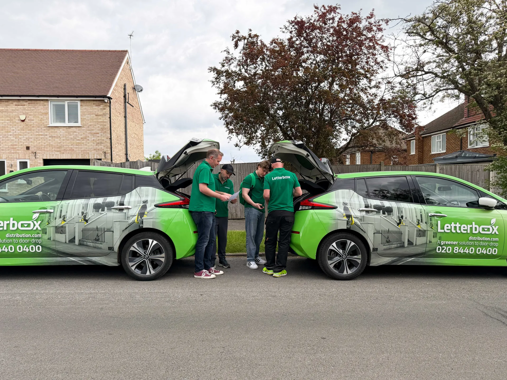 Letterbox door drop team reviewing a delivery round beside branded distribution vehicles